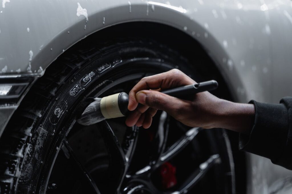 Detailed shot of a hand using a brush to clean a car tire and wheel during a wash.